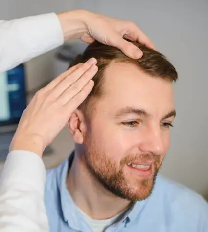 Doctor examining a young man scalp for hair follicles as part of hair transplant consultation